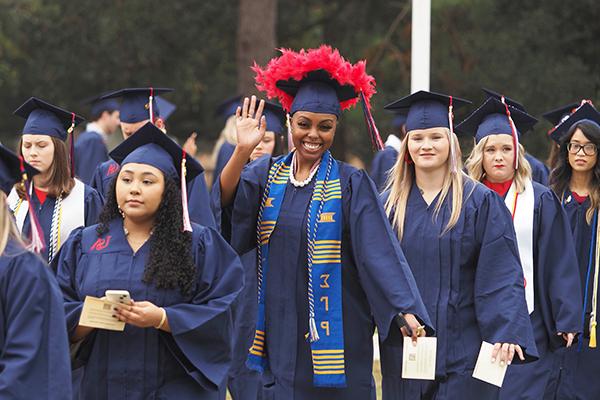 学生 in cap and gowns walking to graduation.